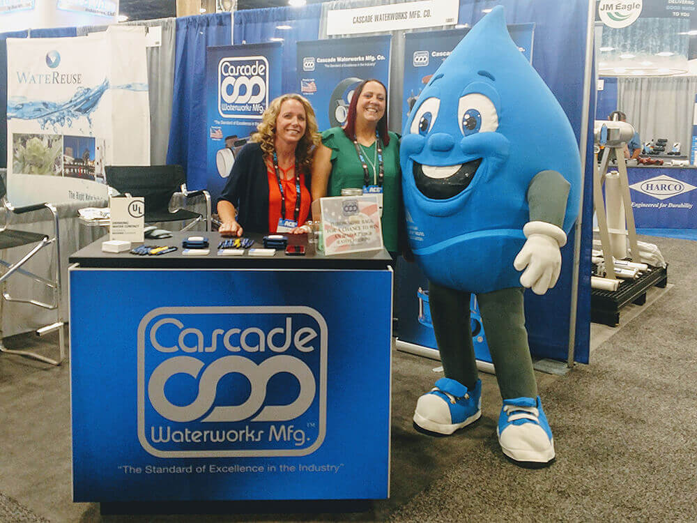 Cascade Employees standing by a booth at a trade show. They are next to a mascot dressed as a water drop.